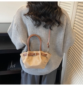 Detail view of beige crossbody bag with brown leather handles on a grey knit sweater