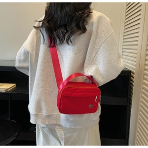 Détail du sac bandoulière rouge en nylon avec large sangle et logo métallique circulaire