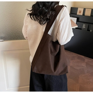 Detail view of large dark brown canvas tote bag with wide strap on shoulder