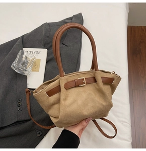 Close-up of khaki suede handbag with brown leather handles and decorative gold buckle detail