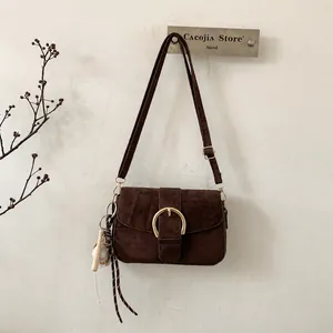 Detail of dark brown suede crossbody bag with gold round buckle and baseball charm