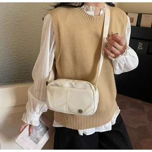 Detail view of a beige nylon crossbody bag with adjustable strap worn by a female model