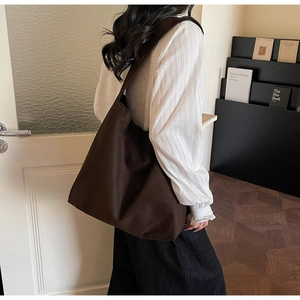 Dettaglio della grande borsa tote in tela marrone indossata da una modella in posa