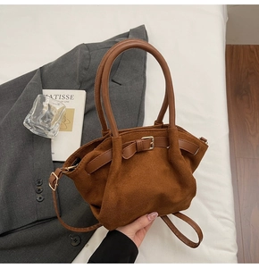 Close-up of brown suede handbag featuring natural pleats and golden metal buckle