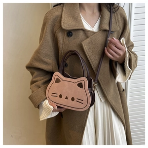 Détail du sac à bandoulière rose en forme de chat porté sur un manteau marron