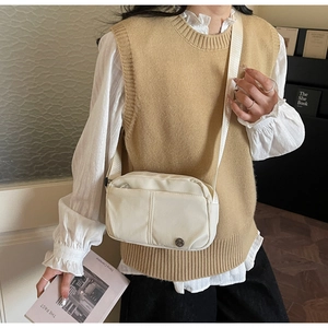 Detail view of cream nylon crossbody bag with front zipper pocket on a female model