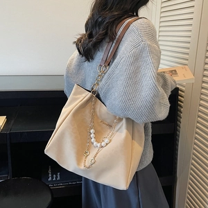 Large beige tote bag with brown straps and pearl chain detail shown on shoulder