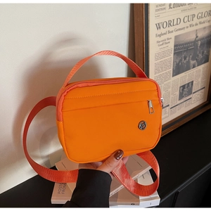 Détail du cabas en nylon orange avec logo rond posé sur des livres blancs empilés