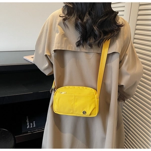 Detail of a bright yellow nylon crossbody bag featuring multiple pockets and wide strap