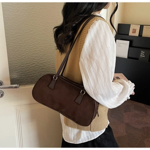 Detail of dark brown suede shoulder bag with dual straps in a cozy studio setting