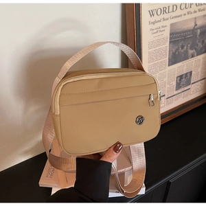 Détail d'un sac bandoulière en nylon kaki avec large sangle et logo métallique sur des livres