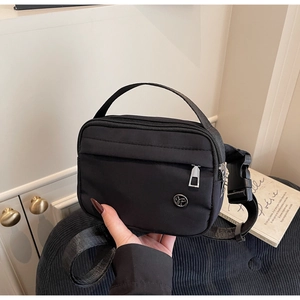 Détail du sac bandoulière en nylon noir avec logo rond et bandoulière réglable