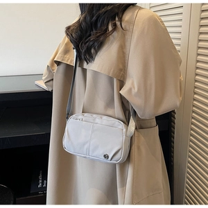Detailed view of light grey nylon crossbody bag shown worn with a stylish trench coat
