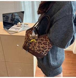 Leopard print bucket bag with bear charm pendant and leather handles on a desktop