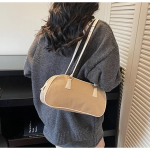 Rear view of a minimalist beige shoulder bag with white trim on a grey knit top