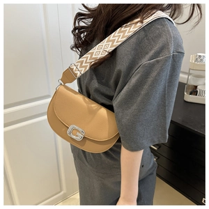 Detail of tan saddle bag with rhinestone G buckle and geometric woven strap on model