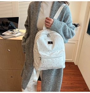 Detail of white backpack featuring silver star patterns and a black brand logo plaque