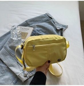 Detail of a bright yellow nylon crossbody bag with metal zipper and adjustable strap