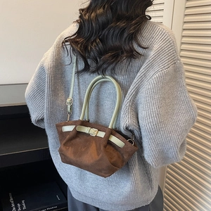 Brown suede retro tote bag with green handles shown on a model in a cozy grey sweater