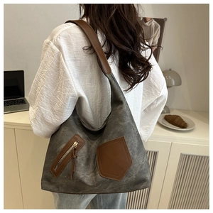 Detail of grey canvas hobo bag featuring brown leather straps and decorative tassel