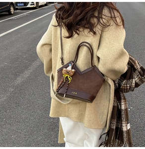 Detail of dark brown bucket bag with JOH logo and cute bear pendant on beige coat