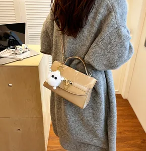 Détail du sac bandoulière en cuir verni beige avec dorures et breloque boule de poil blanc