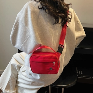 Sac bandoulière minimaliste en nylon rouge avec poche zippée porté par un mannequin