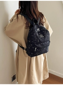 Rear view of a trendy black backpack with white star patterns worn by a model in a room
