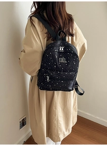 Fashionable black backpack with white star patterns worn over a stylish beige trench coat