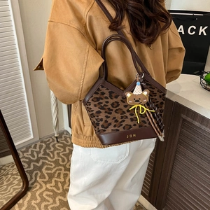 Chic leopard print bucket bag with brown leather trim and cute bear charm worn by a model