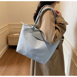 Detail of light blue tote bag featuring flap button closure and golden metal hardware