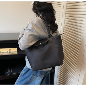 Detail of black nylon tote bag featuring leather handles and secure metal snap closure