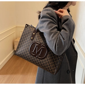Detailed shoulder view of a dark brown large tote bag with M-pattern and relief logo