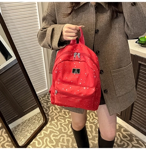 Detail of red backpack with white star patterns and front zip pocket held by model