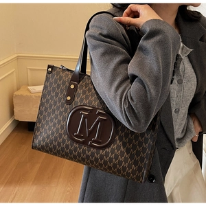 Close-up of brown tote bag with repeating M letter patterns and circular logo detail