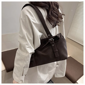 Sac bandoulière marron foncé avec sangle à œillets porté par un mannequin avec élégance