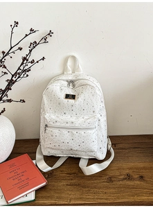 Lifestyle view of a white star-patterned backpack with metal logo on a wooden desk