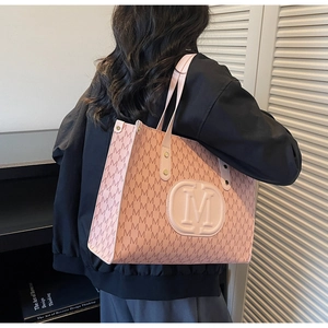 Pink tote bag with all-over M print and metallic studs shown on a model's shoulder