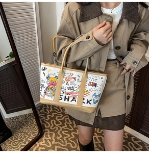 Close-up of a large graffiti tote bag with khaki leather handles on a female model