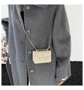 Detail of cream flap crossbody bag with gold chain strap worn with grey tweed coat