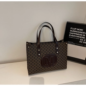 Detail of deep brown leather tote bag with monogram print and embossed M logo emblem