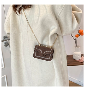 Detail of brown mini crossbody bag with white contrast stitching and gold chain strap