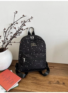 Detail of black backpack with white star patterns and front zipper pocket on wooden desk