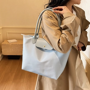 Minimalist light blue nylon tote bag with gray leather handles shown on a model