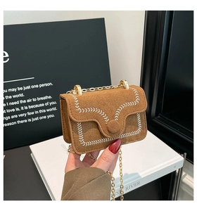 Détail d'un sac bandoulière en daim marron avec broderie blanche et chaîne dorée