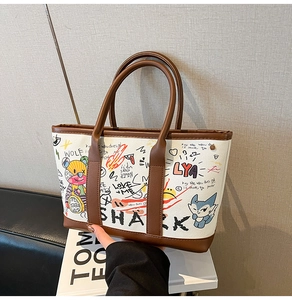 Detail of white canvas tote bag featuring colorful graffiti prints and brown leather handles