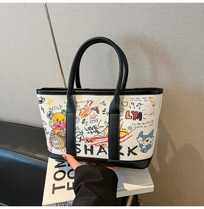 Detail of colorful graffiti canvas tote bag with black leather handles on books