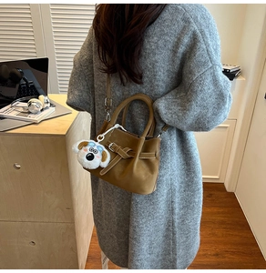 Détail du sac seau en cuir fauve avec breloque chien peluche et bandoulière amovible