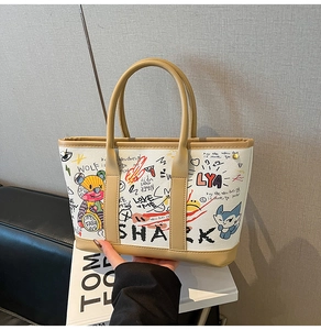 Close-up of white graffiti tote bag with brown leather handles and shark cartoon patterns