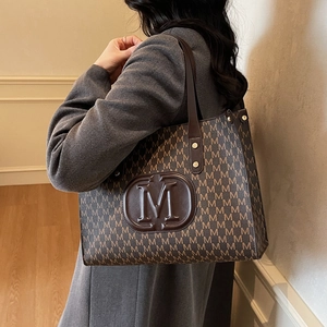 Brown leather tote bag with M-pattern print and large central logo on the shoulder strap